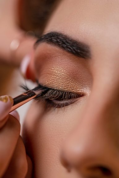 Close-up of an eye with makeup application, featuring false eyelashes and warm eyeshadow.