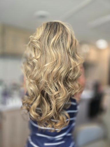 Long, wavy blonde hair cascading down the back, standing in a bright indoor setting, after highlighting.