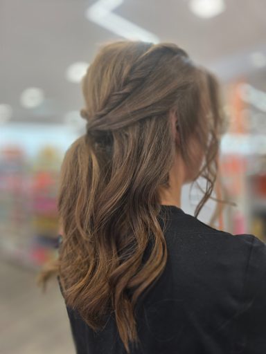 Woman with wavy brown hair styled in a half-up, half-down fashion. Bright background.